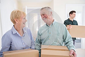 Senior Couple Downsizing In Retirement Carrying Boxes Into New Home On Moving Day With Removal Man Helping