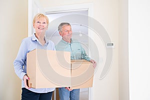 Senior Couple Downsizing In Retirement Carrying Boxes Into New Home On Moving Day photo