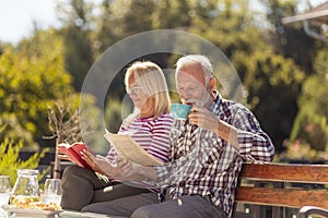 Senior couple drinking morning coffee and reading in the backyard