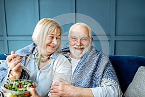 Senior couple eating healthy salad on the couch at home