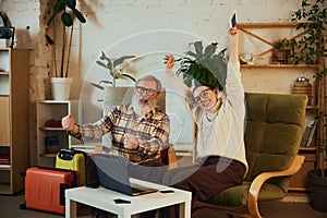 Senior couple, elderly man and woman celebrating successful booking of upcoming trip, sitting with packed luggage