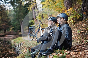 A senior couple with electrobikes sitting outdoors in park in autumn, resting.