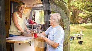 Senior Couple Enjoying Camping In Countryside Relaxing Inside RV And Doing Chores Together