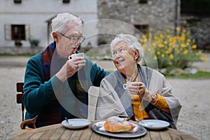 Senior couple enjoying cup of coffee and cake outdoor in cafe.