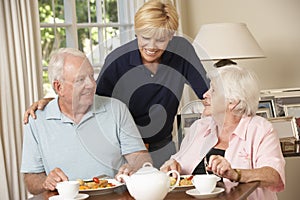 Senior Couple Enjoying Meal Together At Home With Home Help