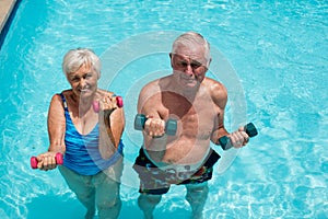 Senior couple exercising with dumbbells in the pool