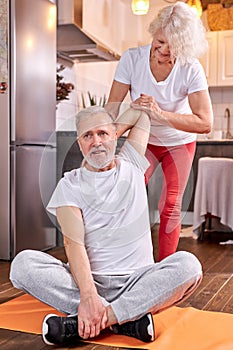 senior couple exercising at home, woman help husband to stretch