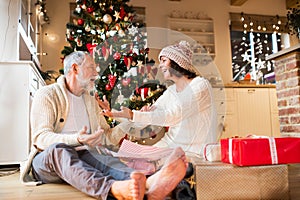 Senior couple in front of Christmas tree enjoying presents.