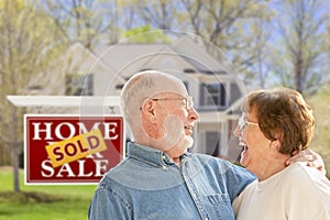 Senior Couple in Front of Sold Real Estate Sign and House