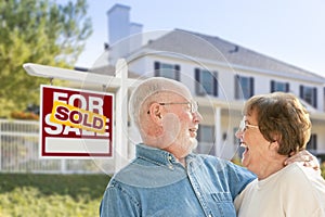 Senior Couple in Front of Sold Real Estate Sign, House