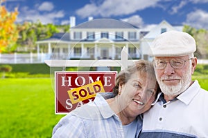 Senior Couple in Front of Sold Real Estate Sign and House