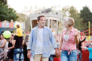 Senior couple at the fun fair, holding hands, walking.