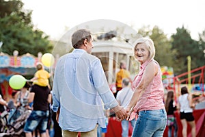 Senior couple at the fun fair, holding hands, walking.