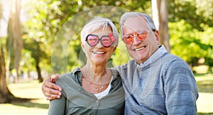 Senior couple, funny glasses and portrait outdoor at a park with love, care and heart shape. A elderly man and woman