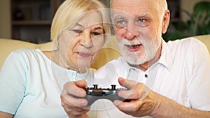 Senior couple gamers playing video games at home. Players with remote controller of game console