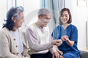 Senior couple get medical service visit from caregiver nurse while using round squishy ball for muscle strength in pension