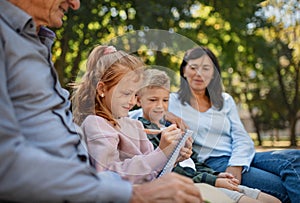 Senior couple with grandchildren sitting on bench and doing homewrok outdoors in park.