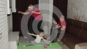 Senior couple with granddaughter using orbitrek, doing weight lifting dumbbells exercises at home