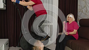 Senior couple with granddaughter using orbitrek, doing weight lifting dumbbells exercises at home