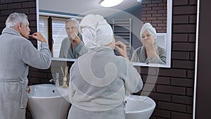 Senior couple grandmother and grandfather brushing teeth and looking into a mirror at bathroom