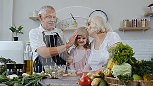 Senior couple grandmother and grandfather in kitchen feeding granddaughter child with chopped pepper