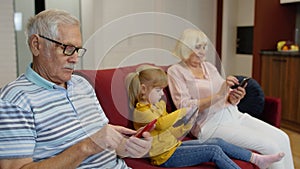 Senior couple grandparents with child girl granddaughter using digital tablet, mobile phone