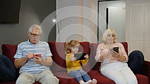 Senior couple grandparents with child girl granddaughter using digital tablet, mobile phone