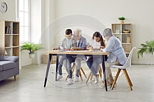 Senior couple grandparents spending time with grandchildren at home drawing at table.