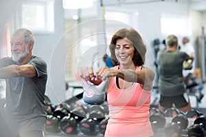 Senior couple in gym working out using kettlebells.