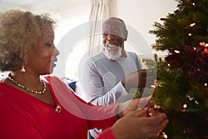 Senior Couple Hanging Decorations On Christmas Tree At Home Together