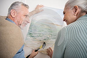 Senior couple hanging together picture on wall at new home