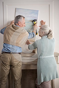 Senior couple hanging together picture on wall at new home