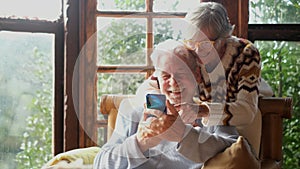 Senior couple have fun together at home using mobile phone to do video conference call to friends or parents. Happy old man and