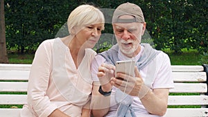 Senior couple have great time sit on bench in park listen to music on smart phone via ear-phones