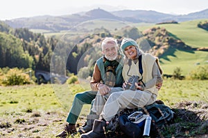 Senior couple having break,sitting with binoculars during hiking in autumn nature.