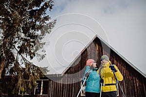 Senior couple having break during skying, next forest cottage.