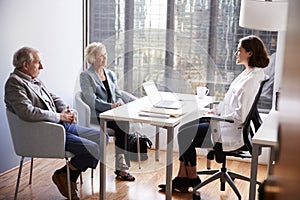 Senior Couple Having Consultation With Female Doctor In Hospital Office