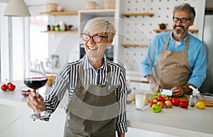 Senior couple having fun, cooking and drinking wine in home kitchen