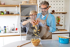 Senior couple having fun, cooking in home kitchen