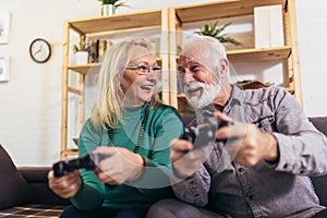 Senior couple having fun at home playing video game holding joysticks in hands.