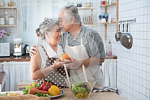 Senior couple having fun in kitchen with healthy food - Retired people cooking meal at home with man and woman preparing lunch