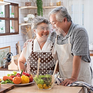 Senior couple having fun in kitchen with healthy food - Retired people cooking meal at home with man and woman preparing lunch