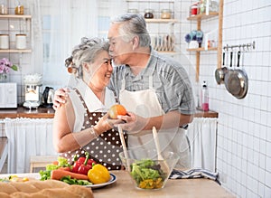 Senior couple having fun in kitchen with healthy food - Retired people cooking meal at home with man and woman preparing lunch
