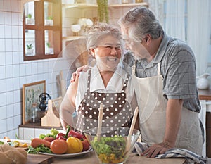 Senior couple having fun in kitchen with healthy food - Retired people cooking meal at home with man and woman preparing lunch