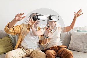 Senior couple having fun with virtual reality glasses, sitting on sofa and gesturing