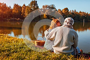 Senior couple having picnic by autumn lake. Happy man and woman enjoying nature and hugging