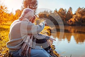 Senior couple having picnic by autumn lake. Happy man and woman enjoying nature and hugging