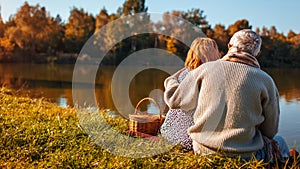 Senior couple having picnic by autumn lake. Happy man and woman enjoying nature and hugging