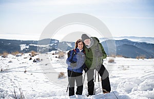 Senior couple hikers with nordic walking poles in snow-covered winter nature.