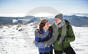 Senior couple hikers with nordic walking poles in snow-covered winter nature.